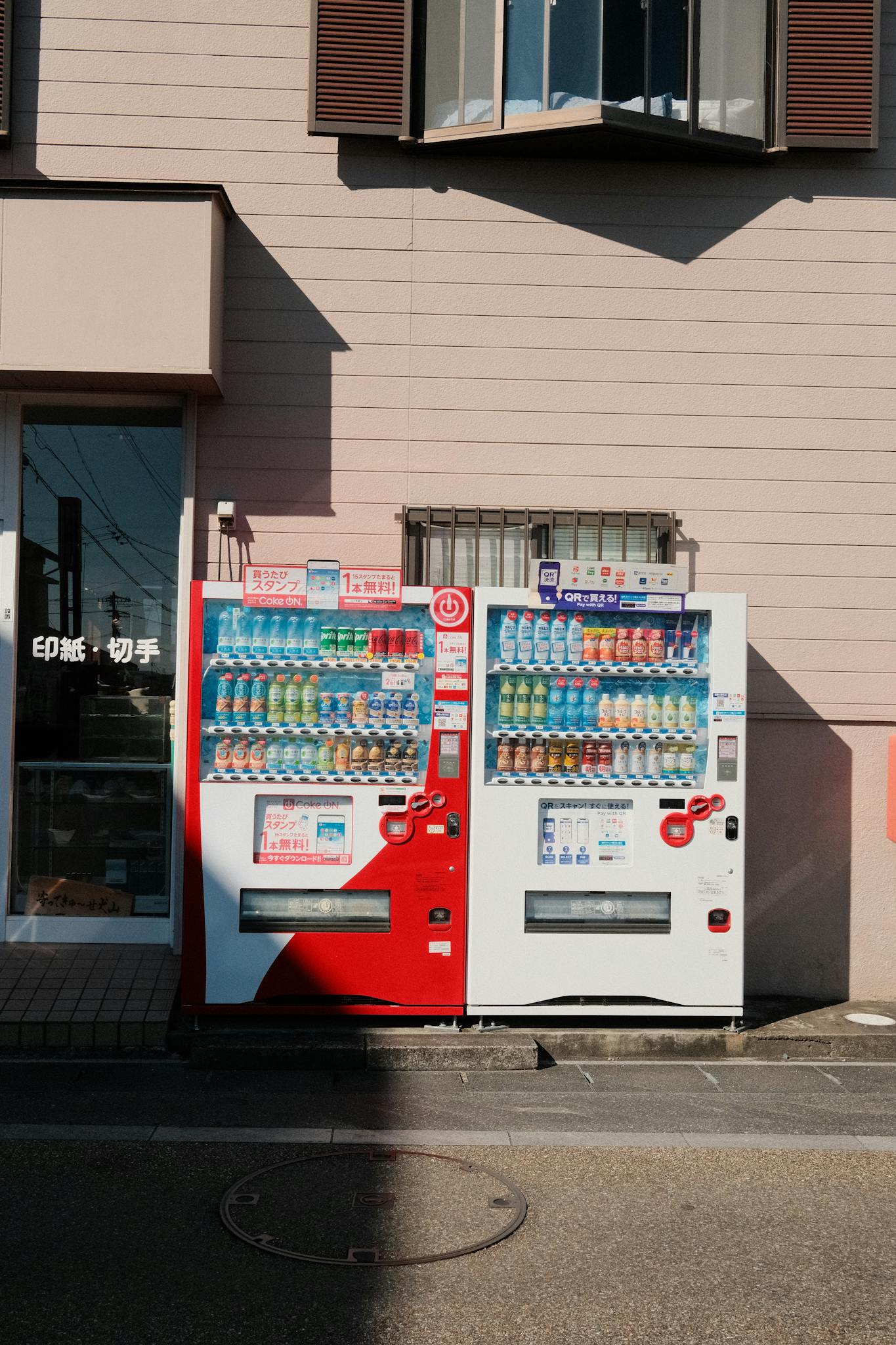 Two colorful vending machines under sunlight in Inuyama, showcasing diverse drink options.
